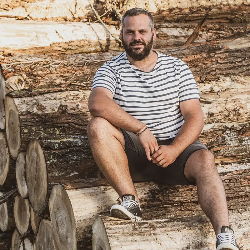 Un homme assis sur des bûches de bois, symbolisant la qualité du bois de chauffage de GV Bois.